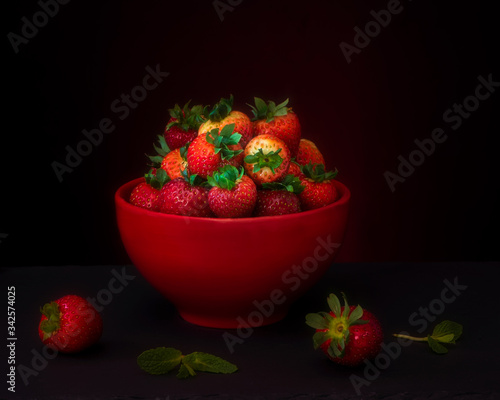 Fresh red strawberries on black background in red ceramic bowl photo