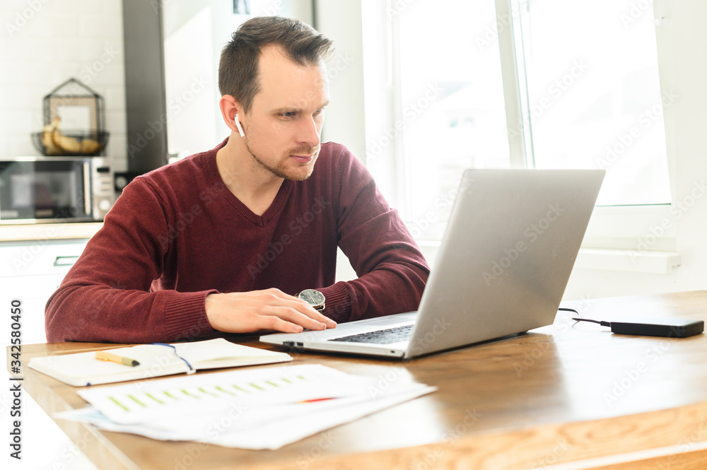 A young concentrated man using laptop to work from home. He is watching on screen with a serious face A young concentrated man using laptop to work from home. He is watching on screen with a serious face