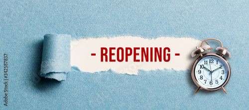 torn paper revealing the word REOPENING on white background photo