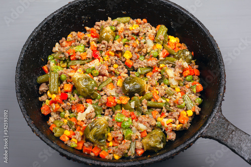 toasted vegetables with minced meat in a cast iron pan, gray background, close up. stew, hearty healthy lunch