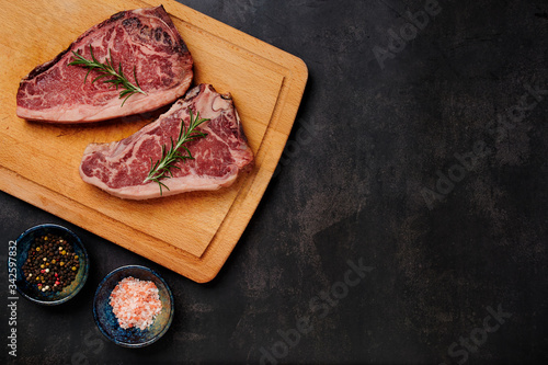 Raw Dry Aged Beef Steak. Raw Dry Aged Meat. Raw sirloin steak on a wooden board with four peppers blend, himalayan salt, and rosemary. black slate stone background