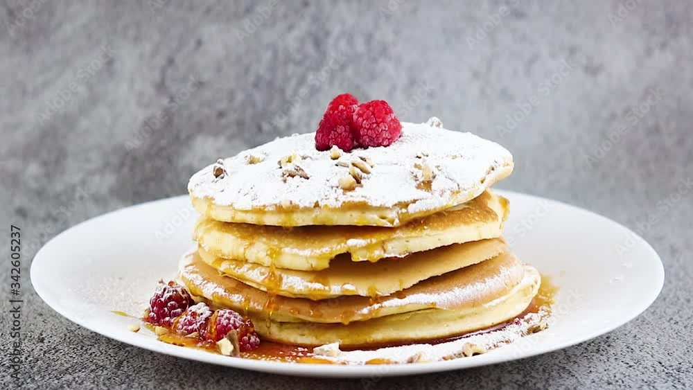 Delicious pancakes decorated with raspberries, maple syrup and powder sugar on white plate Delicious pancakes decorated with raspberries, maple syrup and powder sugar on white plate