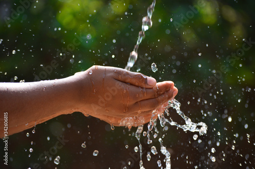 Water pouring in kid two hand on nature background. Hands with water splash.