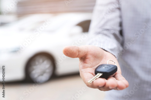 Car key, businessman handing over gives the car key to the other man on car background.	