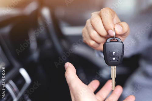 Car key, businessman handing over gives the car key to the other woman on showroom background.