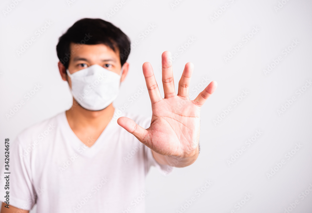 Closeup Asian handsome Man wearing surgical hygienic protective cloth face mask against coronavirus and raising hand stop sign, studio shot isolated white background, COVID-19 medical concept Closeup Asian handsome Man wearing surgical hygienic protective cloth face mask against coronavirus and raising hand stop sign, studio shot isolated white background, COVID-19 medical concept