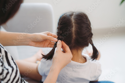 Young loving mother brushing kid daughters hair sitting on sofa,
