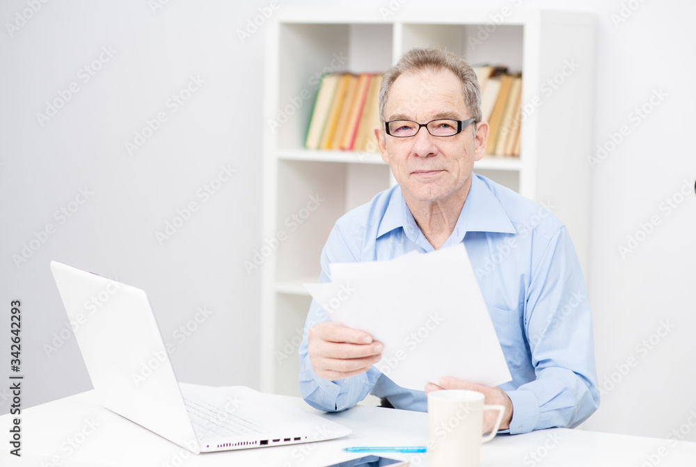 Serious senior gentleman at laptop computer browsing internet sitting in modern office. Work life in older age. Selective focus