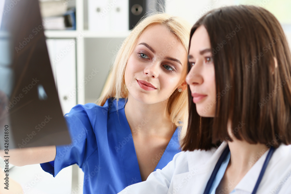 Group of beautiful female doctors hold in hand and look at xray photography to detect problem. Bone disease exam, medic assistance, cancer aid, healthy lifestyle, ill test, hospital practice concept Group of beautiful female doctors hold in hand and look at xray photography to detect problem. Bone disease exam, medic assistance, cancer aid, healthy lifestyle, ill test, hospital practice concept
