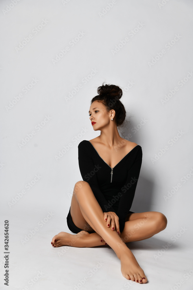 Sensual brunette woman in black dress is sitting against the wall with her legs tucked up looking aside Sensual brunette woman in black dress is sitting against the wall with her legs tucked up looking aside