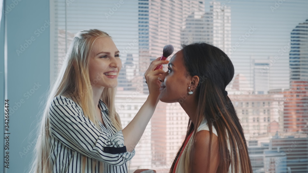 Fototapeta premium Close-up of make-up artist applying makeup on black model with skyscrapers in the background. They preparing for fashion magazine photo shoot.