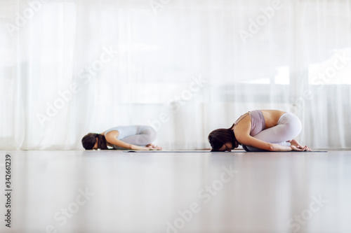 Two fit dedicated yogi women in Child's yoga pose. Yoga studio interior.