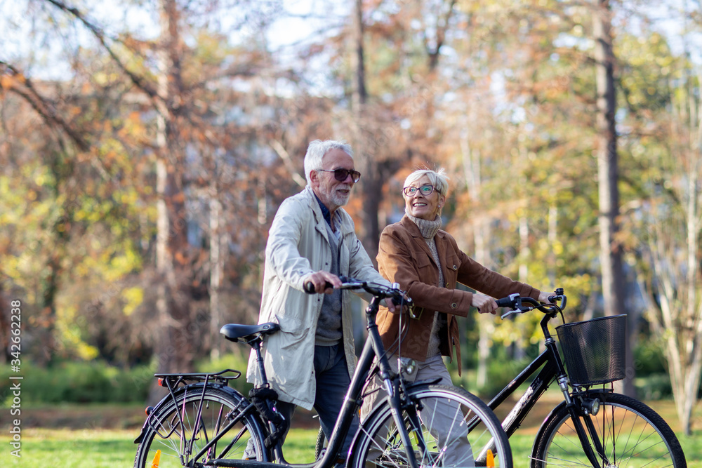 Obraz premium Mature fit couple pushing bicycles in public park talk and smile