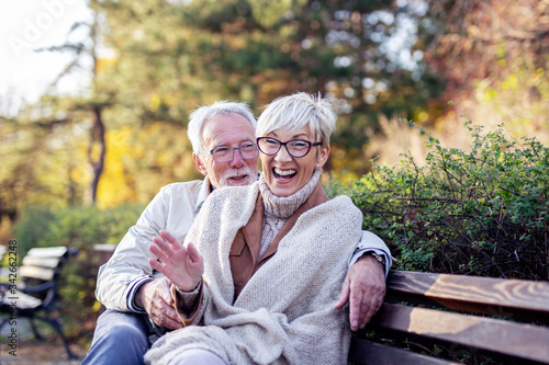 Mature couple sitting on bench in public park talk and smile