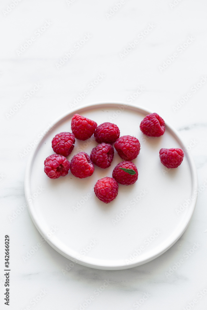 Plate of Fresh Raspberries on white marble background with copy space Plate of Fresh Raspberries on white marble background with copy space