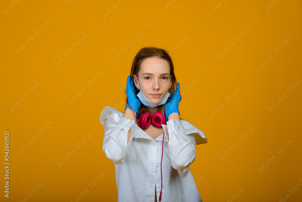 The caucasian girl in blue colored protective face mask. The girl looking at camera. Portrait shot over yellow background. virus and pollution protection concept. The caucasian girl in blue colored protective face mask. The girl looking at camera. Portrait shot over yellow background. virus and pollution protection concept.