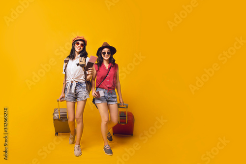 Asian women got tickets to travel promotion on summer  Two young girl traveller holding suitcase and passport in studio.