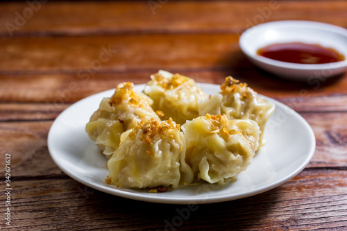 Chinese Steamed Dumpling, Shumai on white dish served with soy sauce on wooden table. Delicious Dimsum pork.