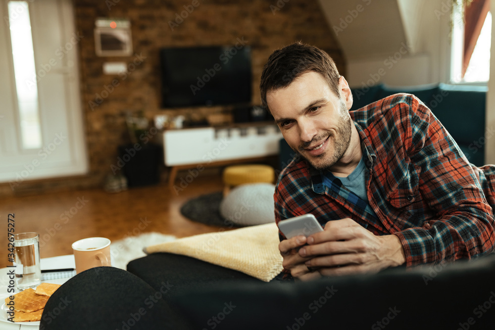 Happy man typing text message on cell phone while relaxing in the living room Happy man typing text message on cell phone while relaxing in the living room