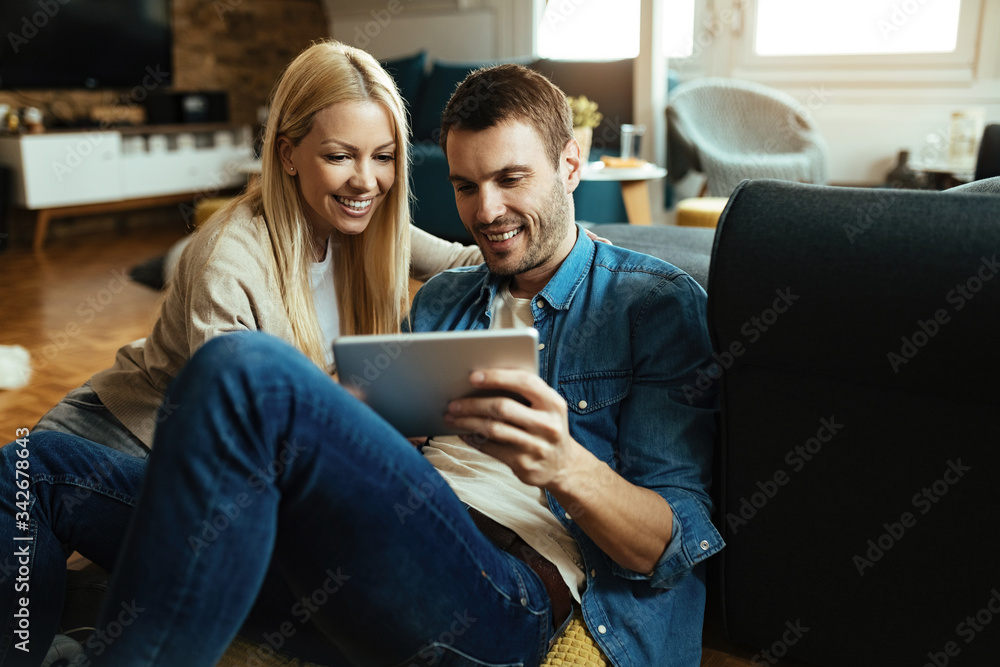 Happy couple using digital tablet while relaxing in the living room.