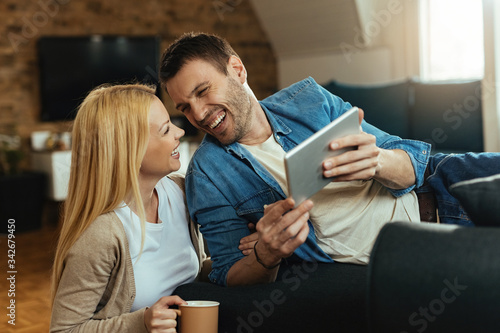 Cheerful couple laughing while using digital tablet at home.