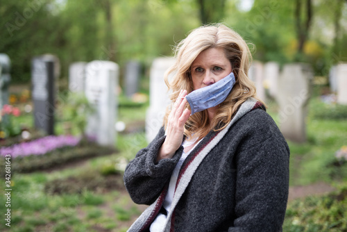 Frau mit Atemmaske auf dem Friedhof, Trauer zur Zeit des Coronavirus 