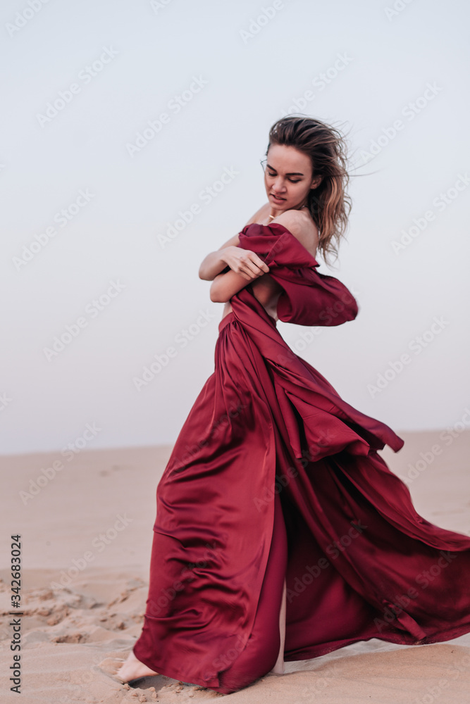 Girl with fabric stands in the wind in the desert