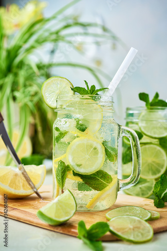 A glass of homemade lemon, lime, and mint lemonade sits on the wooden dining table. Cold, refreshing summer lemonade or mojito.