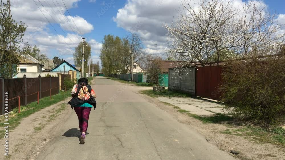 Senior active woman running along road on empty street in village or suburban. Sport on quarantine and self-isolation in Ukraine. Overall plan. Senior active woman running along road on empty street in village or suburban. Sport on quarantine and self-isolation in Ukraine. Overall plan.