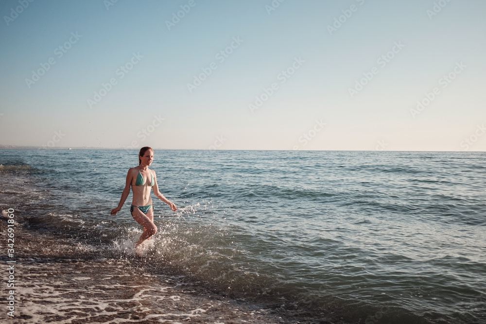 Girl in a bikini runs along the waves on the beach in summer