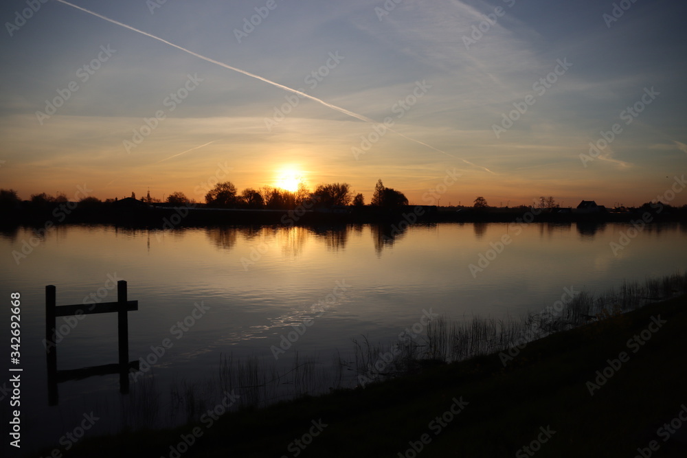 The sun rises over the water of the river Hollandsche IJssel near the dike at Park Hitland