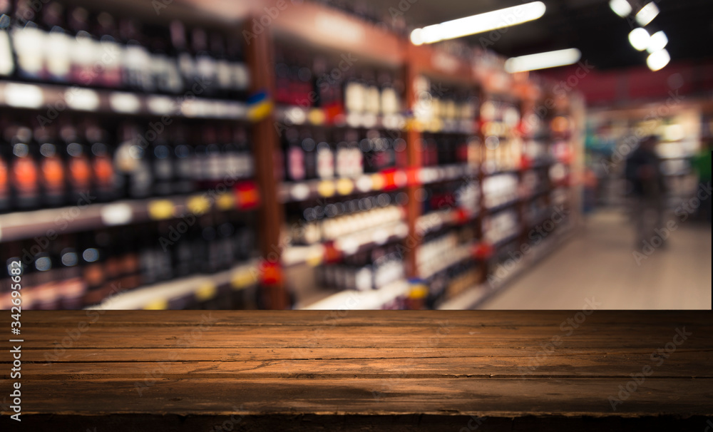 Bartender or male cavist standing near the shelves of wine bottles holds a glass of wine, looks at tint and smells flavor of wine in glass.