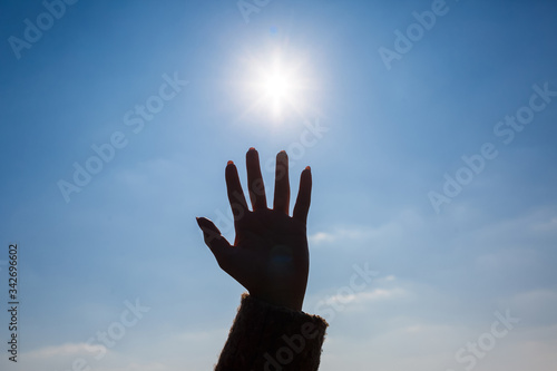 silhouetted a female hand against a blue sky and bright sun