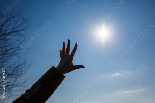 silhouetted a female hand against a blue sky and bright sun