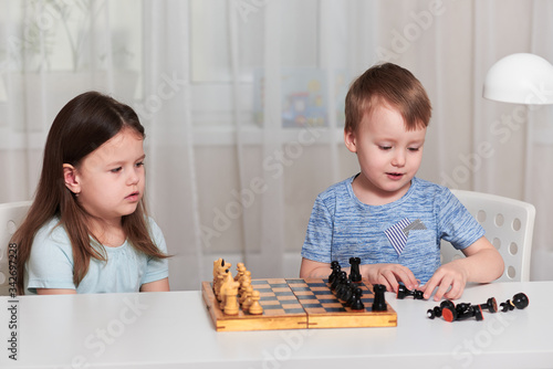 A little girl and a boy sit at a table and play chess