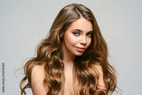 Portrait of young beautiful woman isolated at grey background. Blonde girl with long and shiny wavy hair . Smiling friendly girl with curly hairstyle