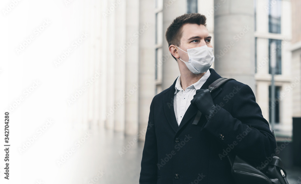 Businessman and coronavirus epidemic. Close up portrait of young business man in a disposable facial mask. A man defends himself against covid 19 on the big city street. Modern buildings at background Businessman and coronavirus epidemic. Close up portrait of young business man in a disposable facial mask. A man defends himself against covid 19 on the big city street. Modern buildings at background