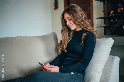 Giovane bella ragazza studente/ lavoratrice studia/ lavora da casa con il telefono. Smart working e distanza sociale. Lavorare con la tecnologia, social network e svago photo