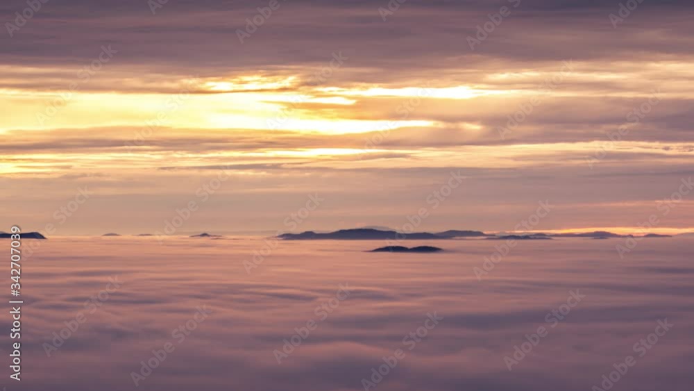 Zoom out time lapse over inversion clouds. Low fog clouds moving over basin. In distance visible hills above mist. Amazing colorful sunrise golden hour over Slovenia landscape Zoom out time lapse over inversion clouds. Low fog clouds moving over basin. In distance visible hills above mist. Amazing colorful sunrise golden hour over Slovenia landscape