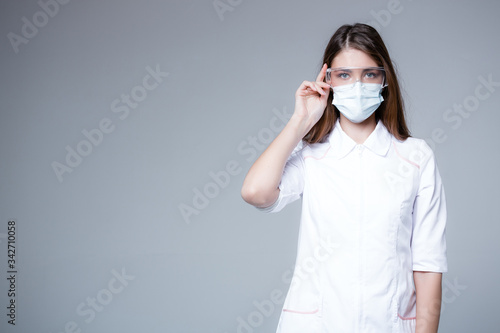 Infectionist doctor in transparent glasses and a medical mask looks into the frame. Protector doctor concept on gray background