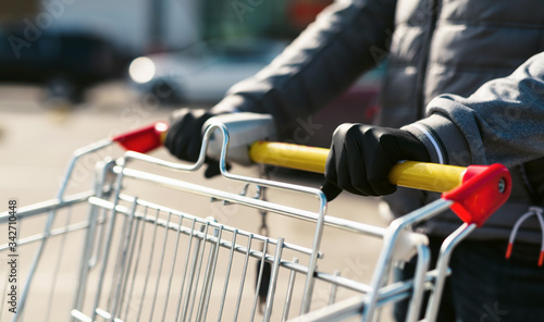 Coronavirus 2020 pandemic. Close up of man hands in medical disposable gloves with a supermarket cart. People goes to the market to buy food during quarantine. Covid 19 epidemic over the World