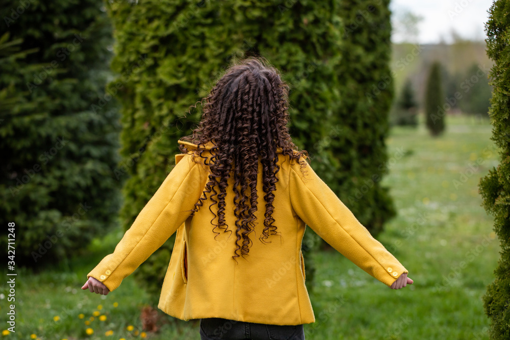 Fototapeta premium Young woman rests in the park in spring. Curly brunette in a yellow jacket