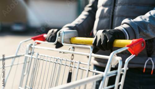 Coronavirus 2020 pandemic. Close up of man hands in medical disposable gloves with a supermarket cart. People goes to the market to buy food during quarantine. Covid 19 epidemic over the World