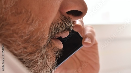 Close-up of the mouth of a bearded man talking on a smarphone. Communication technology concept.