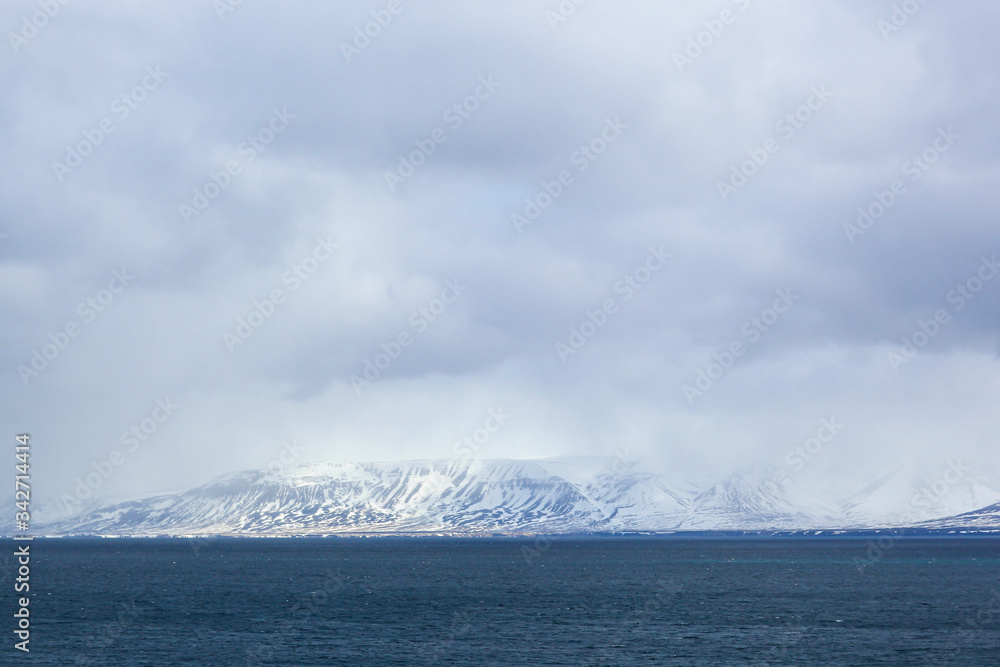 Snow-covered mountain in the middle of the ocean. Rain gloomy sky