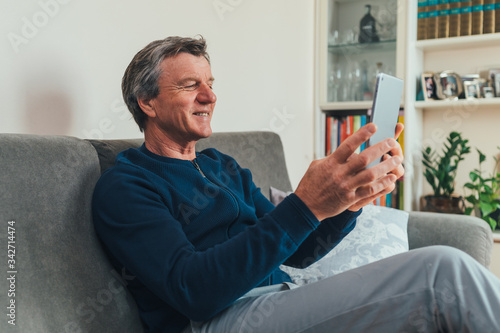Uomo di mezza età/ anziano realizza una video chiamata con il tablet da casa  photo