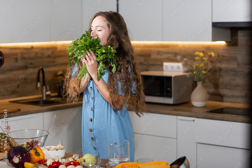 Woman in kitchen holding green fresh aromatic parsley leaves. Young housewife in jeans dress cooking. Healthy eating, vegetarian food, dieting and people concept. for weight loss and detox. Vertical