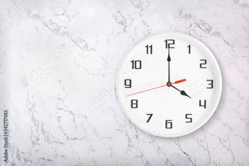 White round wall clock on white natural marble background. Four o'clock, 4 a.m. or 4 p.m.
