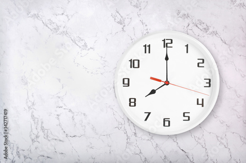 White round wall clock on white natural marble background. Eight o'clock, 8 a.m. or 8 p.m.