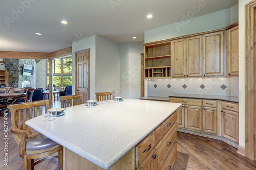 Bright wooden large kitchen interior with island with three chairs and white grey backsplash.